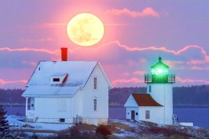 the full moon rises behind the Curtis Island Lighthouse