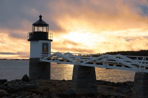 Golden light dances on the clouds behind Marshall Point Lighthouse.