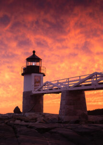 An orange sky behind Marshall Point Lighthouse at sunset.